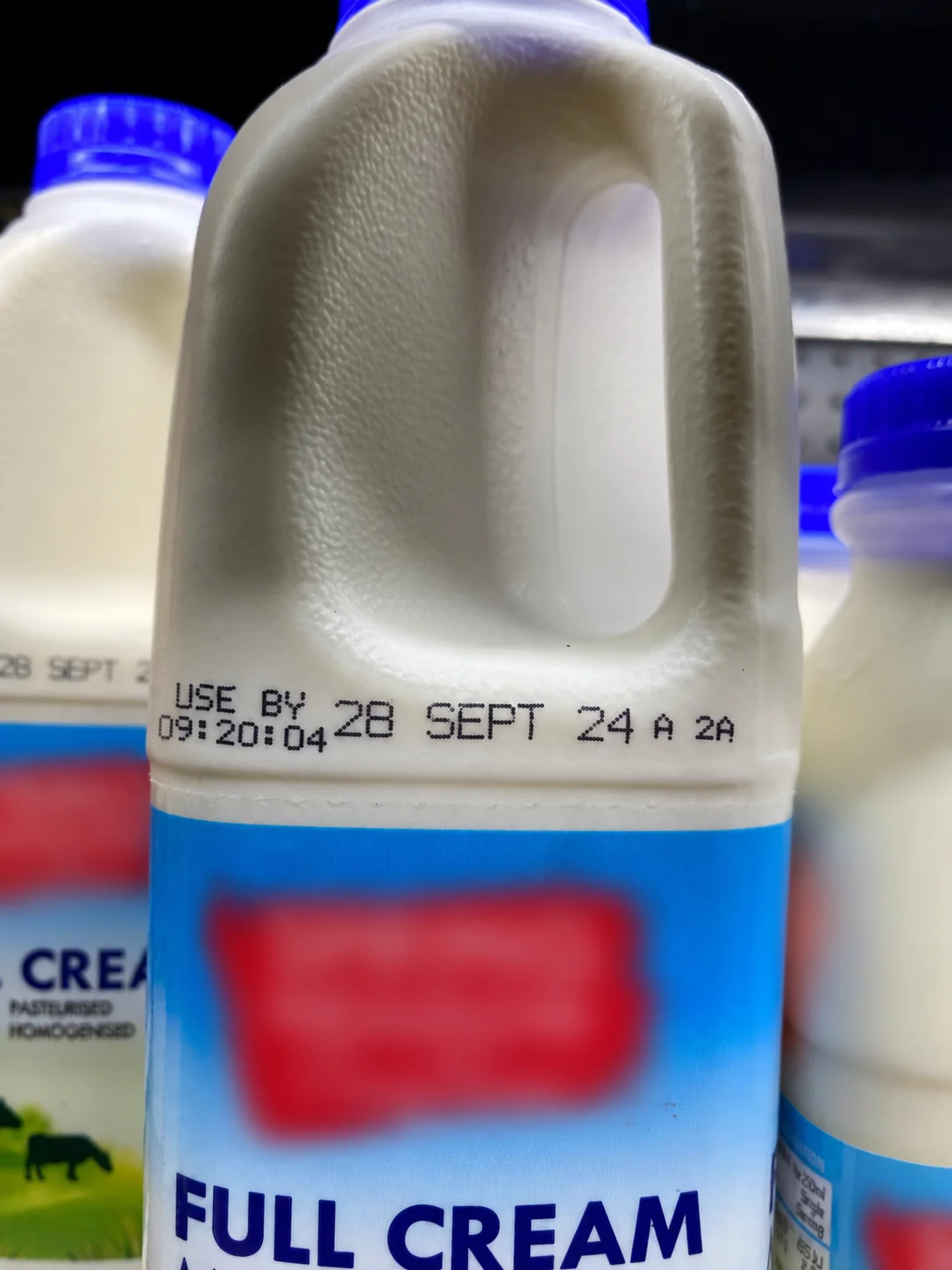 Clear Hitachi UX-B date code on a refrigerated 2 L HDPE milk bottle in store